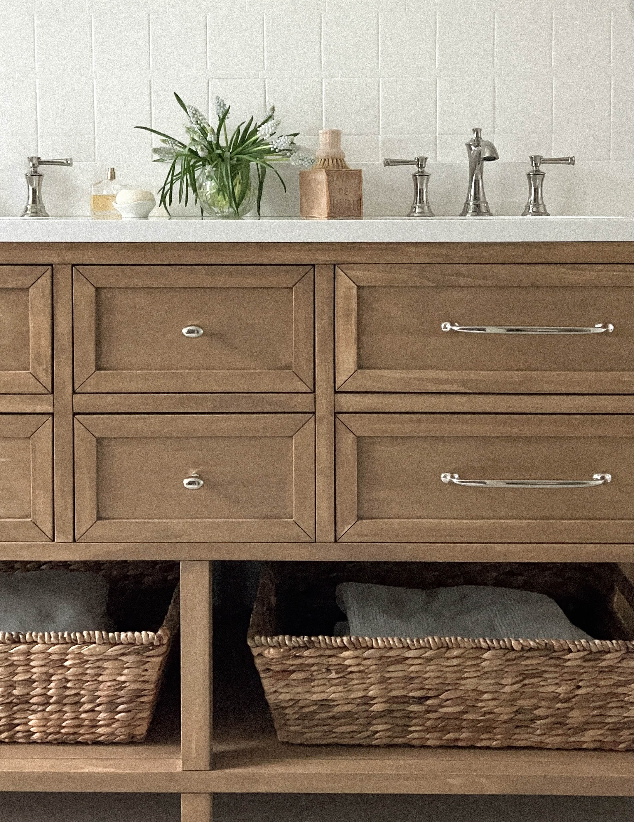Wooden bathroom vanity with drawers, baskets, and decorative items.